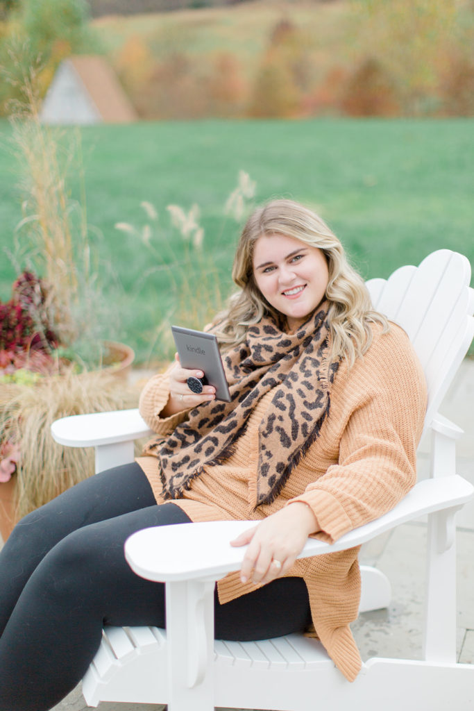 smiling plus size woman reading a kindle and wearing plus size leggings and a camel sweater