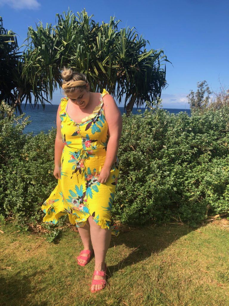 A blonde woman wearing a yellow floral midi dress as a plus size vacation outfit. 