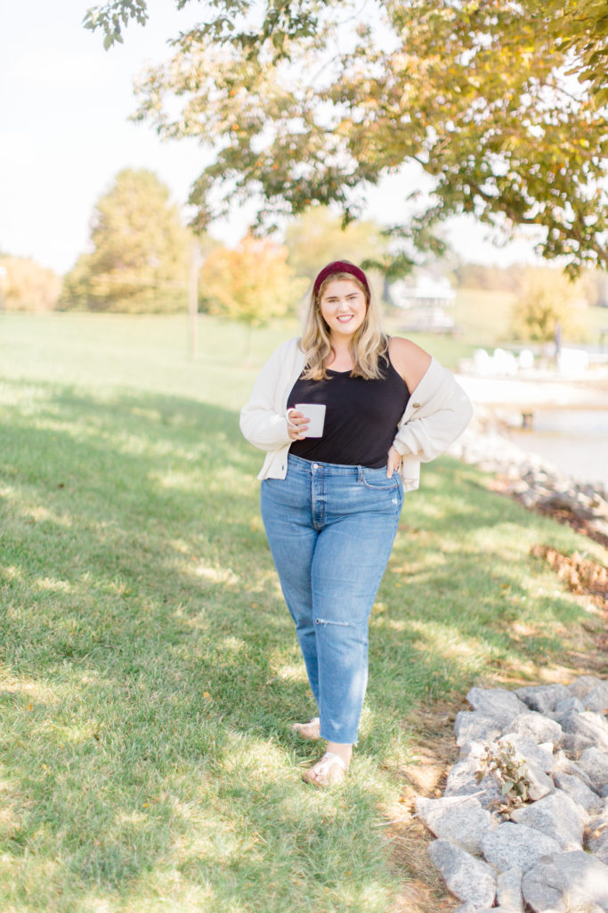 blonde woman standing outside in the grass wearing plus size jeans, a black tank top and a cream cardigan