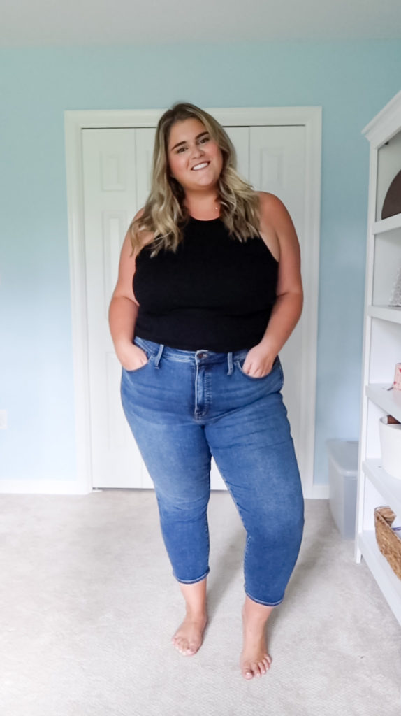 a blonde woman wearing the best plus size jeans and a black tank top standing in her room