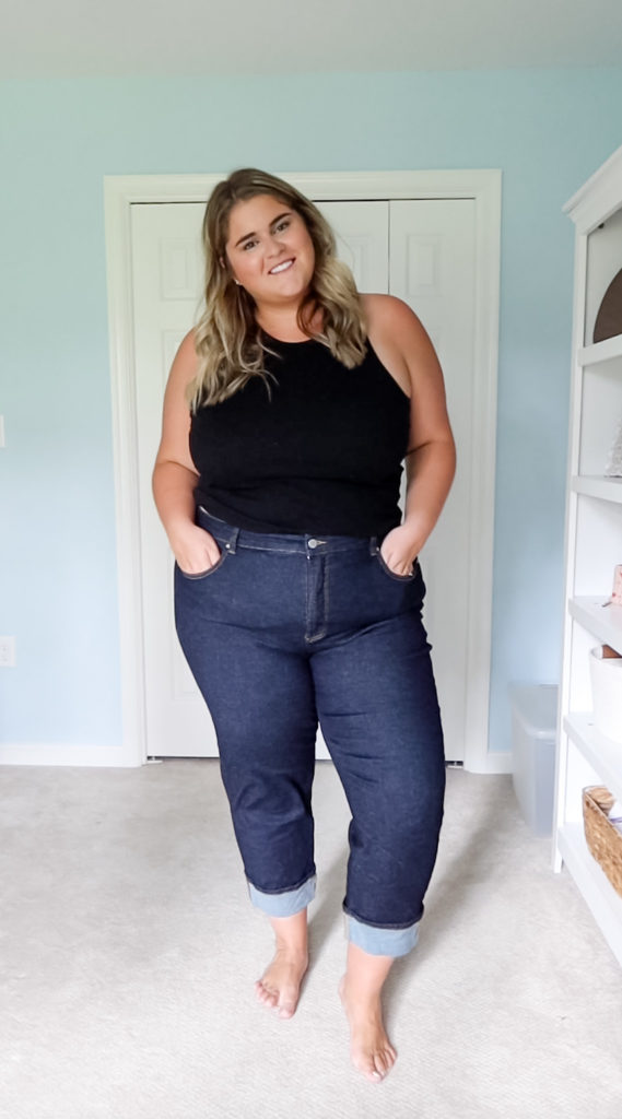 a blonde woman wearing a pair of dark jeans and a black tank top standing in her room