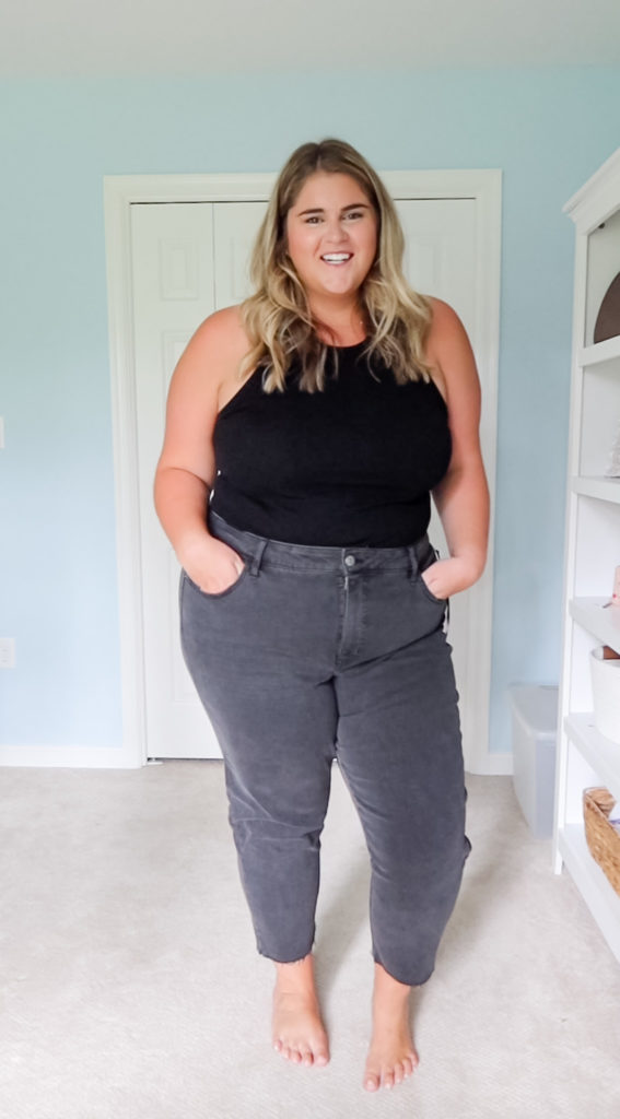 a happy woman with blonde hair wearing black jeans and a black tank top in her room