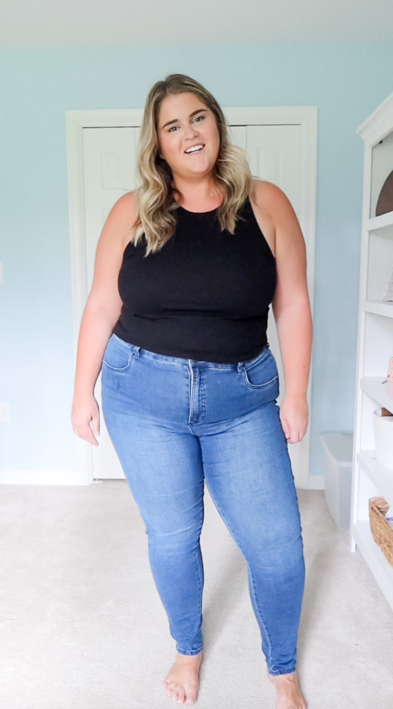 a happy blonde woman wearing the best plus size jeans and a black tank top