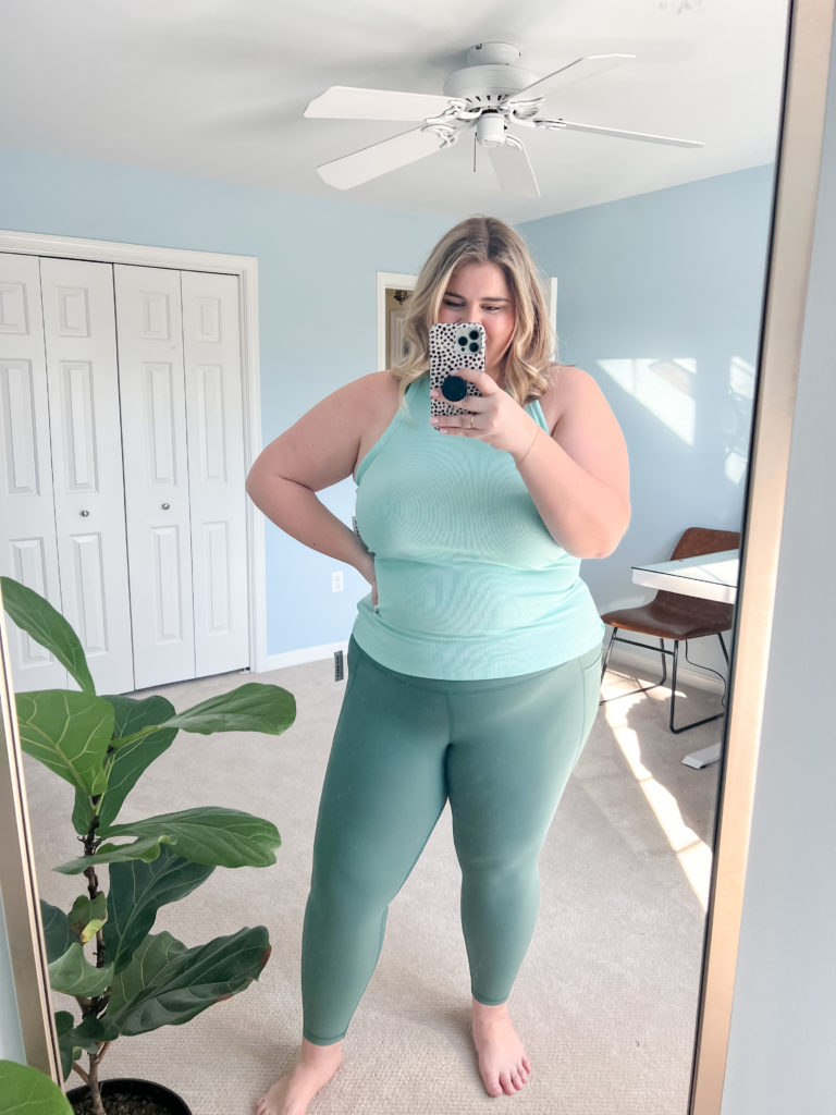 happy blonde woman wearing plus size leggings outfit of sage leggings and teal tank top