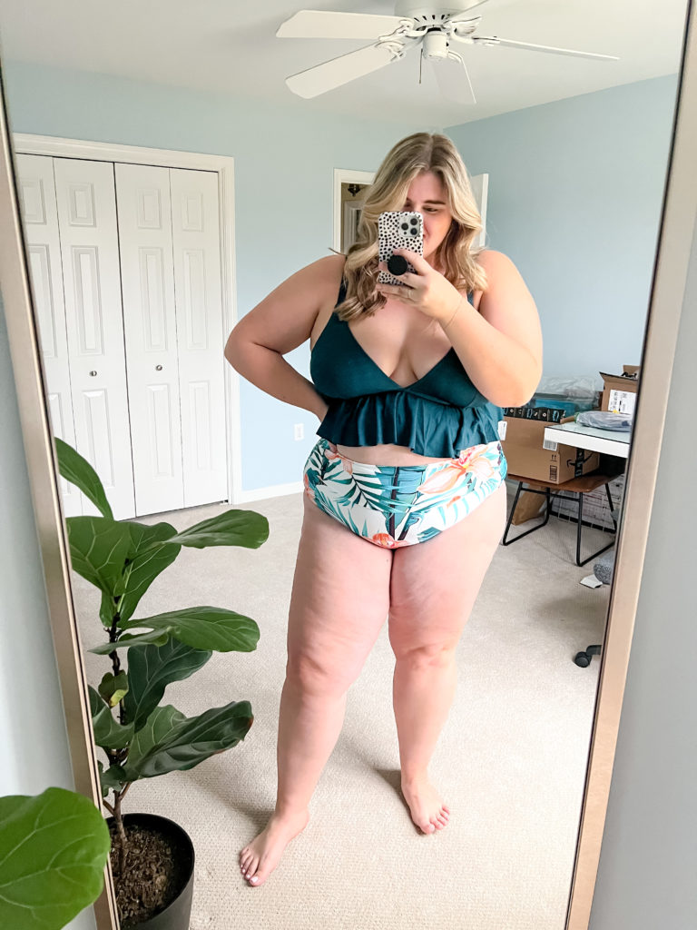 A smiling blonde woman wearing an Amazon plus size bikini that is teal on top and floral design on bottom. 