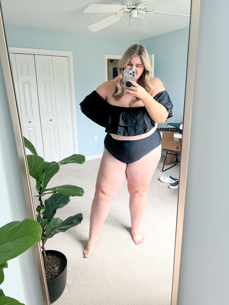 A plus size Caucasian woman wearing an Amazon black ruffle bikini in her bedroom while taking a mirror selfie. 