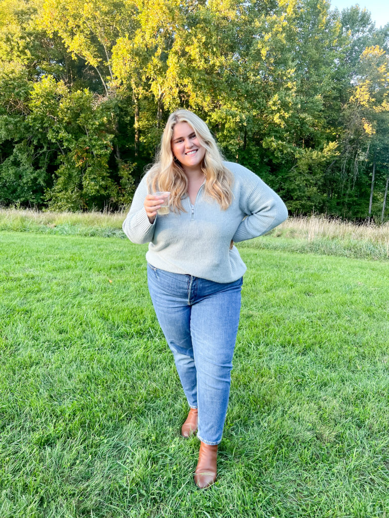 a blonde woman holding a cup of cider outside wearing the best plus size jeans