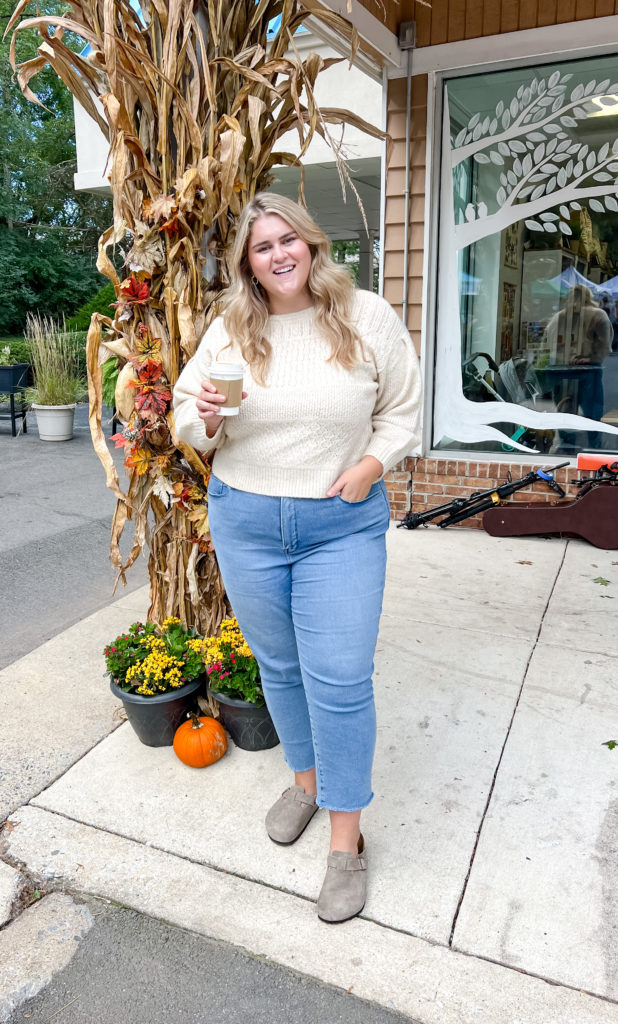 a happy Caucasian woman wearing Birkenstocks and straight leg jeans outside near a restaurant holding coffee  