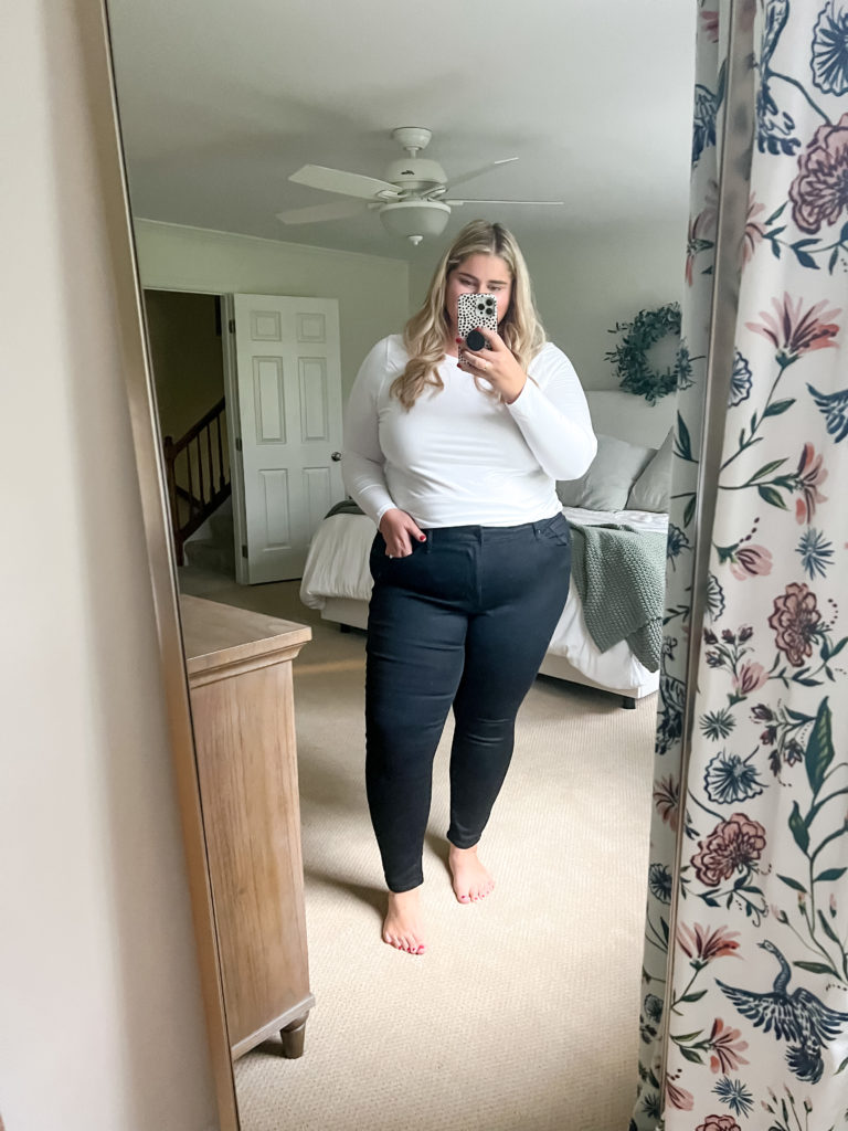 blonde woman wearing a white shirt and black jeans taking a mirror selfie