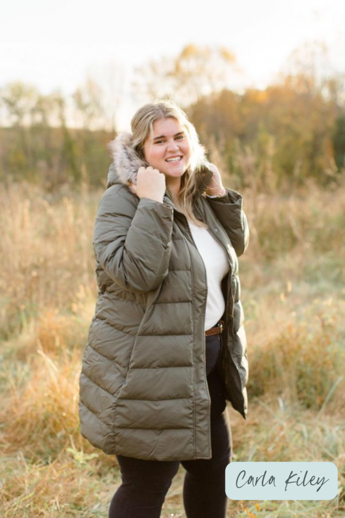 A plus-size Caucasian woman is standing in a field and posing for a picture wearing an olive puffer coat from Lands' End. 