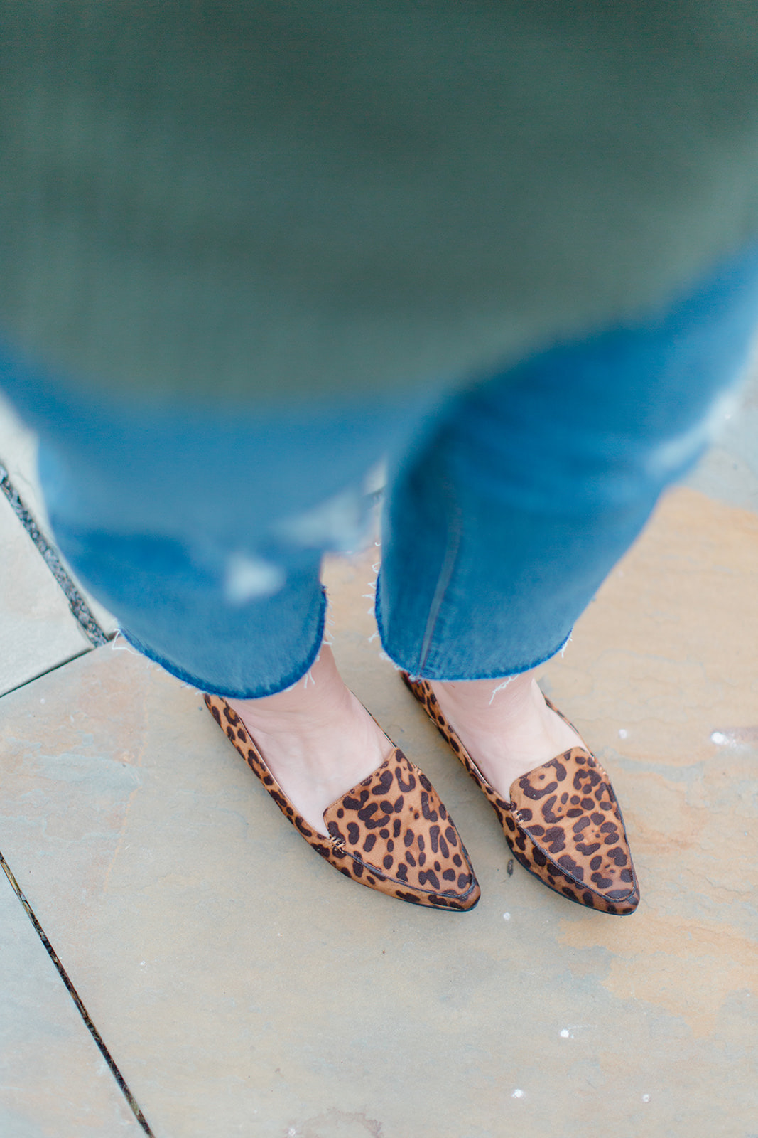 a woman's legs in straight leg jeans and leopard loafers