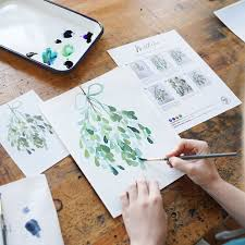 a Caucasian hand painting a watercolor picture of mistletoe

