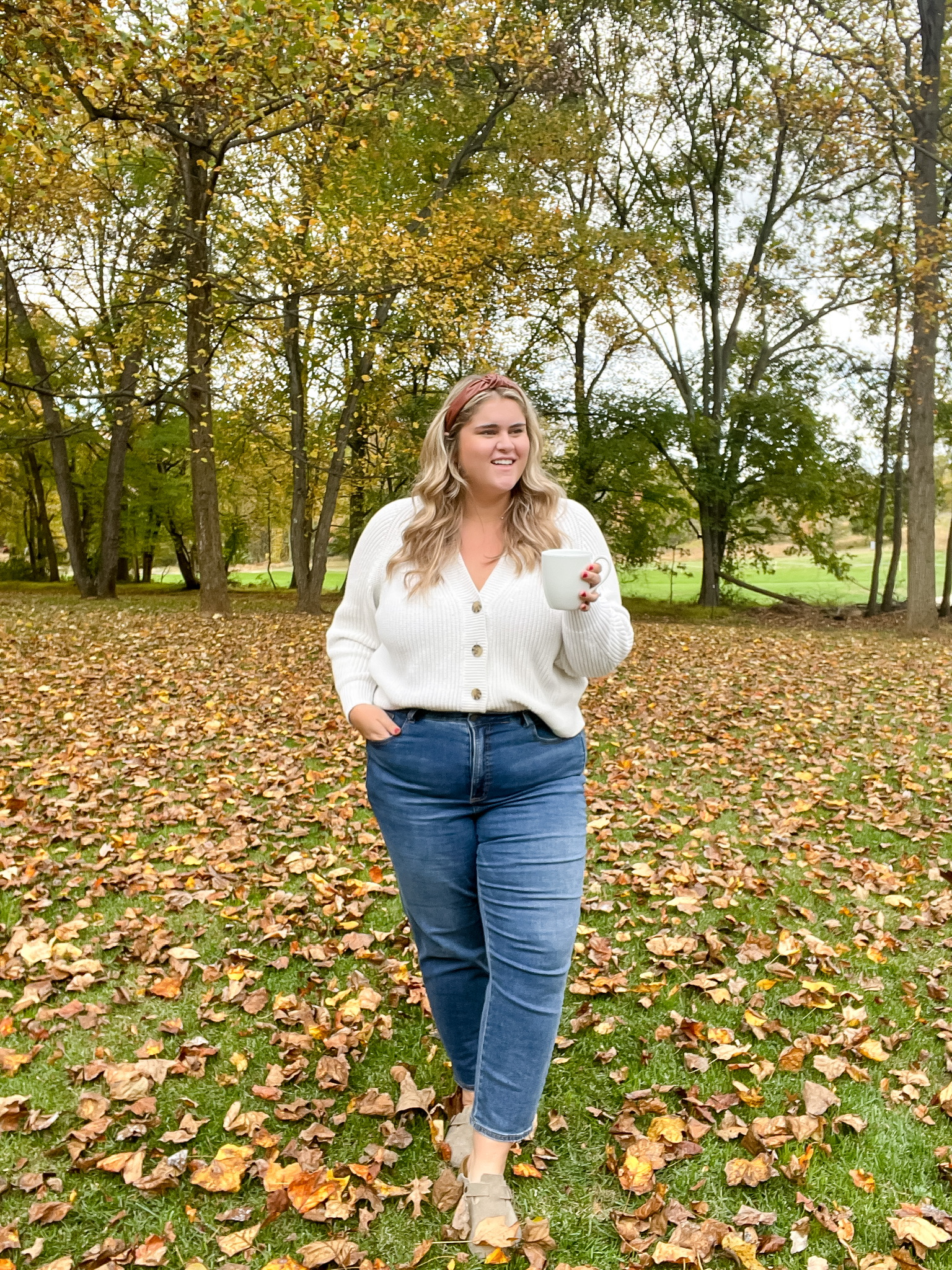 a blonde woman modeling in the woods wearing a cream sweater and Birkenstock Shoes With Straight Leg Jeans