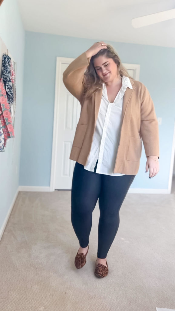 plus size woman wearing black leggings, a white button down and camel cardigan