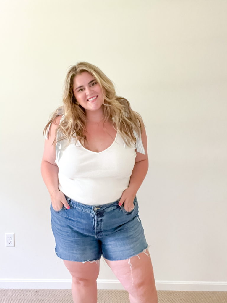 smiling plus size white woman wearing a white tank and denim cutoff shorts