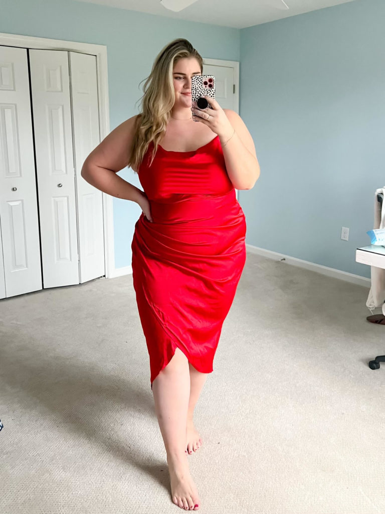 a plus size Caucasian woman wearing a red slip dress taking a mirror selfie