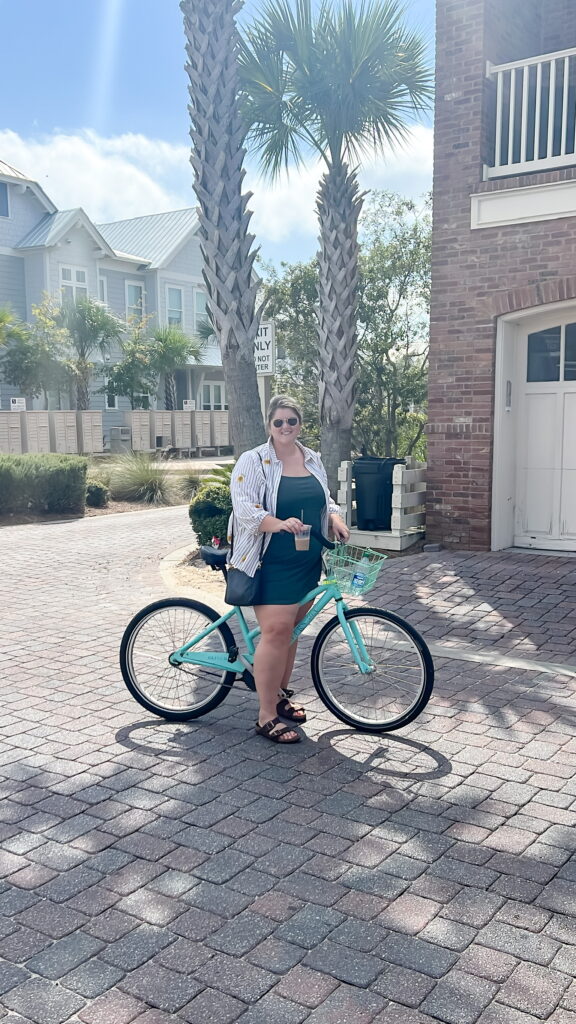 A happy plus size Caucasian woman is posing for a picture outside, on her bike ,while wearing a vacation outfit. 