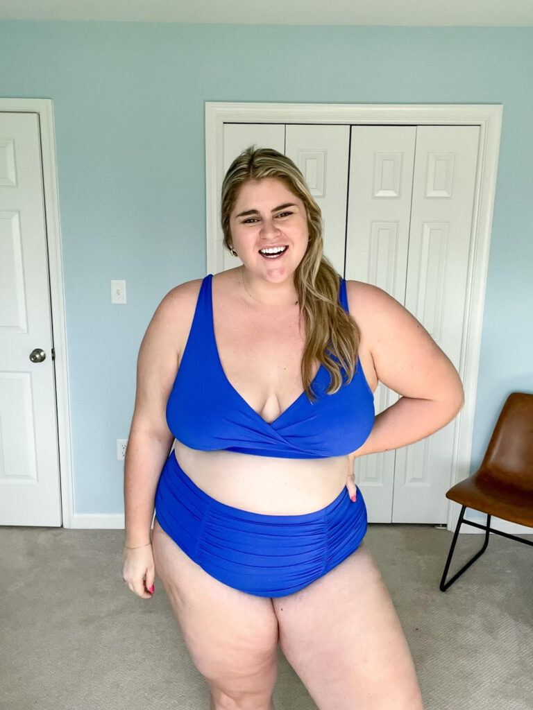 Smiling Caucasian woman modeling a blue plus size Amazon bikini in her bedroom.