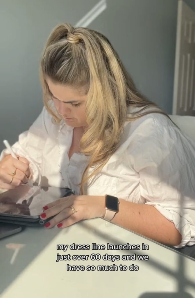 Blonde Caucasian woman wearing a white shirt is designing a dress on her iPad. 