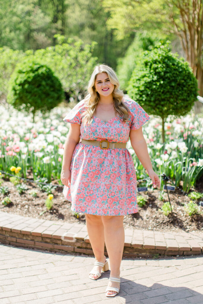 Pretty blonde woman beaming with joy in a rose printed cotton dress, striking a pose outside.