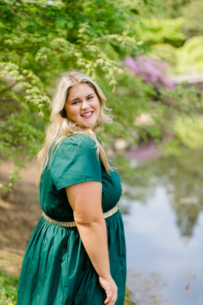 Plus size blonde woman looking radiant in an emerald green dress, enjoying a sunny day outdoors